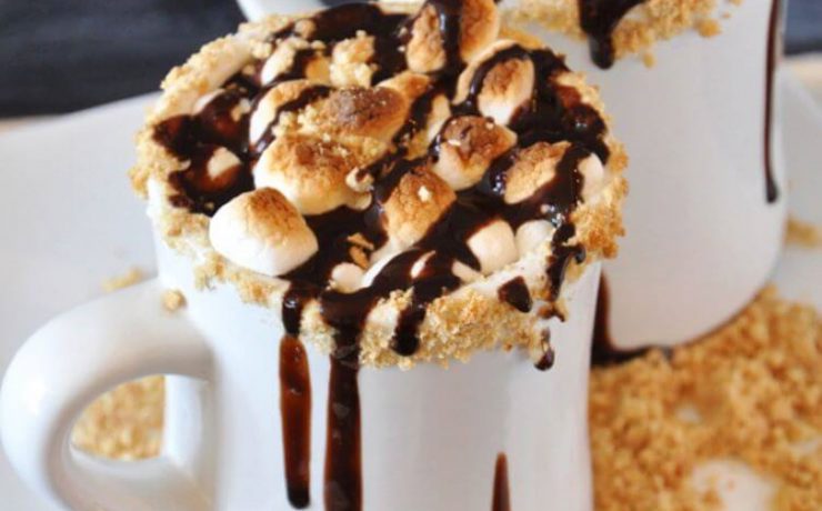 Gooey marshmallows clump together in a cup of hot chocolate brimming with chocolate syrup and gram cracker shavings.