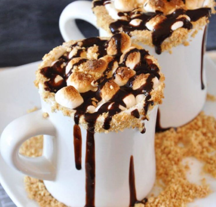 Gooey marshmallows clump together in a cup of hot chocolate brimming with chocolate syrup and gram cracker shavings.