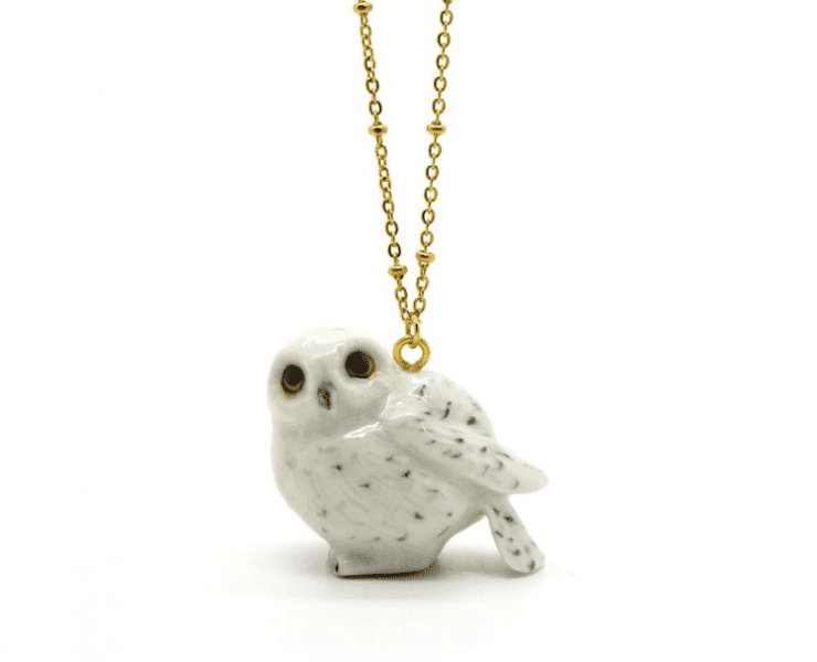 Snow owl pendant hanging from a gold necklace. The owl is made of porcelain