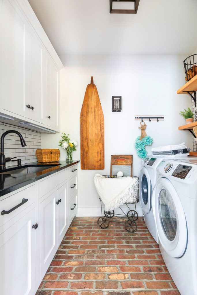 The white laundry room has a wood ironing board that folds onto the wall and the sink has white backsplash