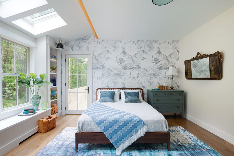 The master bedroom with white and blue floral accent wall. In front of the accent wall sits a queen size bed and blue chest of drawers