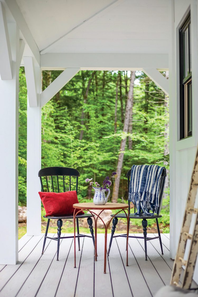 Two chairs and a mini table with a jug on the porch to our Project House