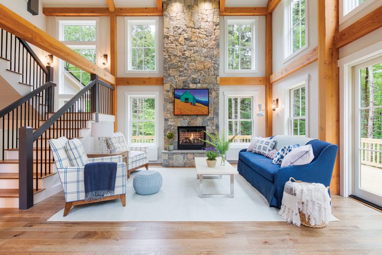 A large fireplace made from stones reaches the Project House's vaulted ceiling. The room has many wood paneling in light, blonde wood