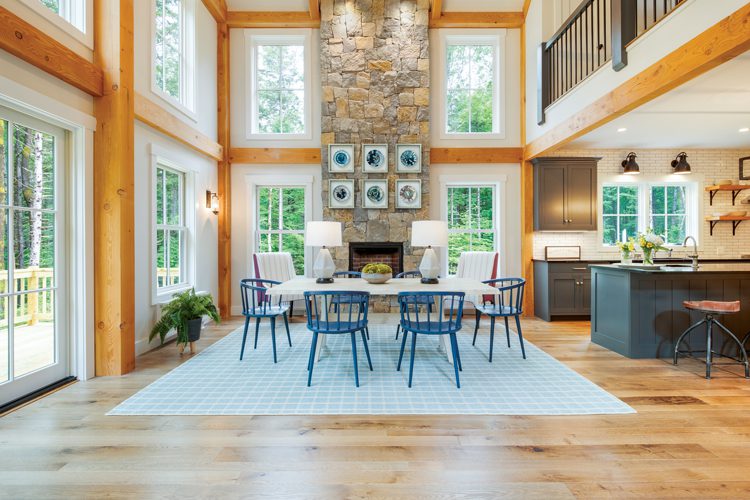 A large fireplace made from stones reaches the Project House's vaulted ceiling. The room has many wood paneling in light, blonde wood