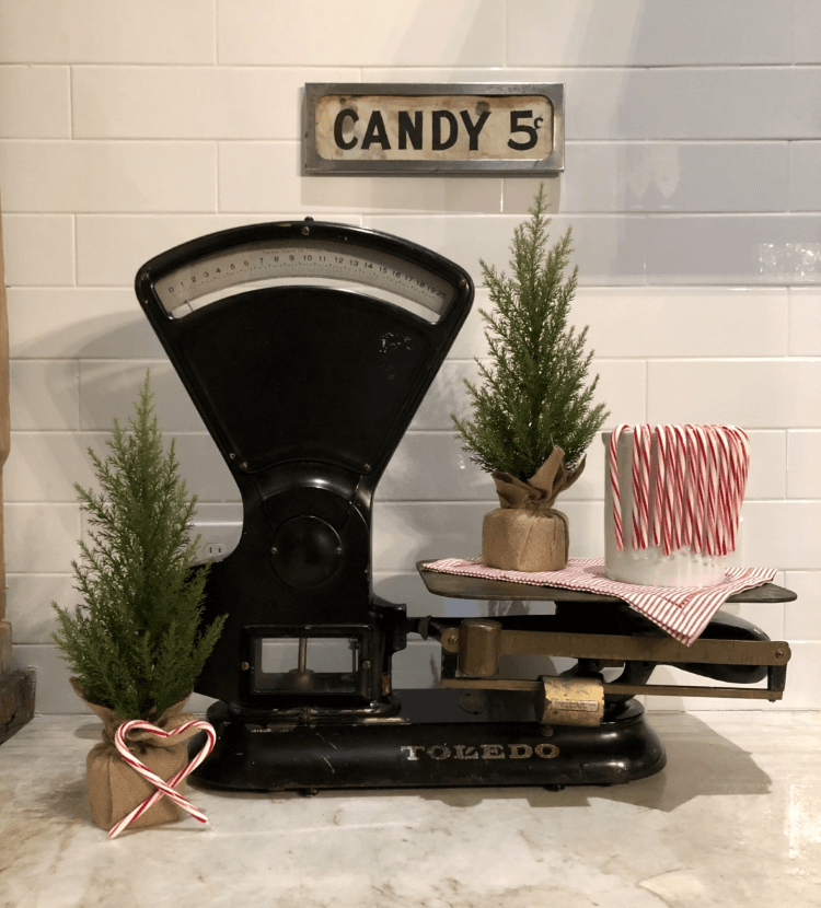 An antique weigher with mini Christmas trees and a jar of candy canes on top.