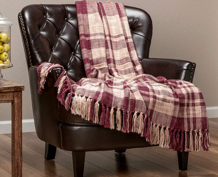 Red plaid decor throw blanket with tassels draped over a leather chair.