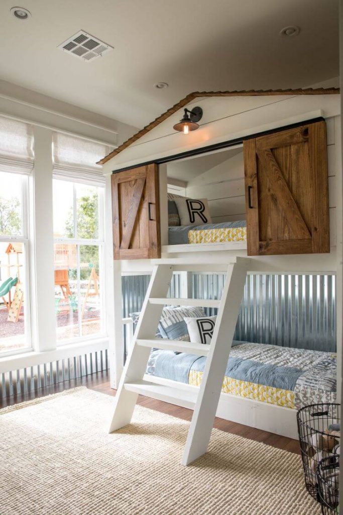 A child's bunkbed with the top bunk resembling a barn. Sliding barn doors open to reveal a child's bed. The room has stunning aluminum walls.