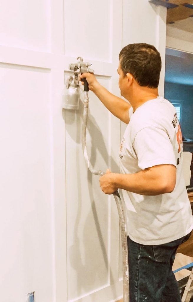 A man uses a paint sprayer to evenly spray white paint on the boards