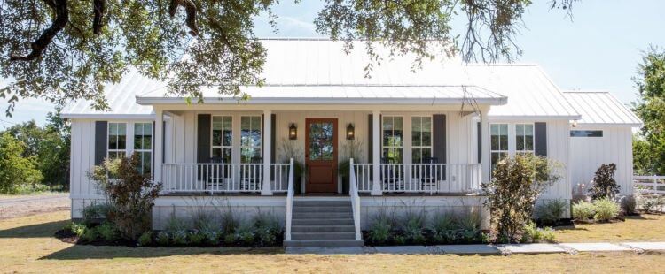 A beautiful white house with dark shutters and white farmhouse style roof