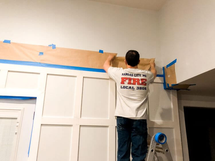 A man adds papers and blue tape arounds areas not being painted