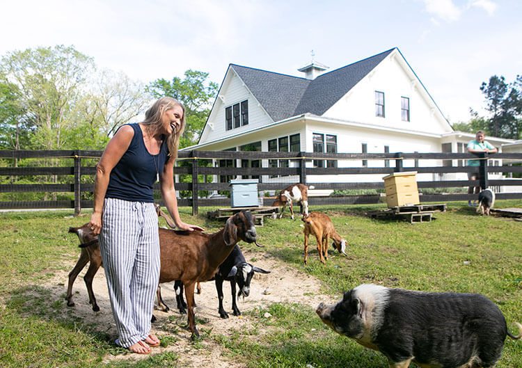 Woman petting goat outside farmhouse with pig