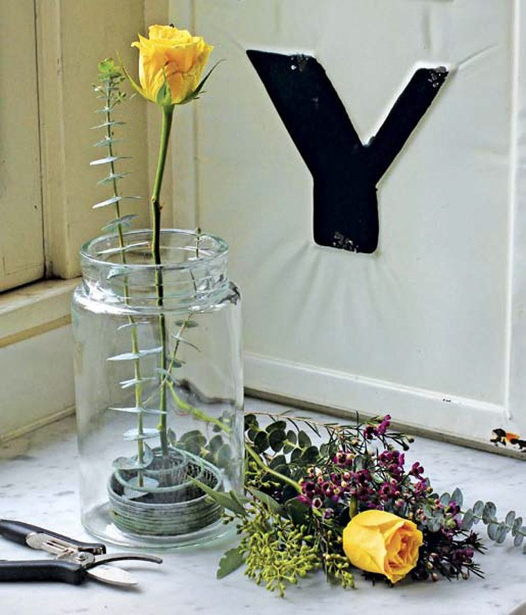 A flower frog sits inside a glass mason jar near a bundle of different flowers