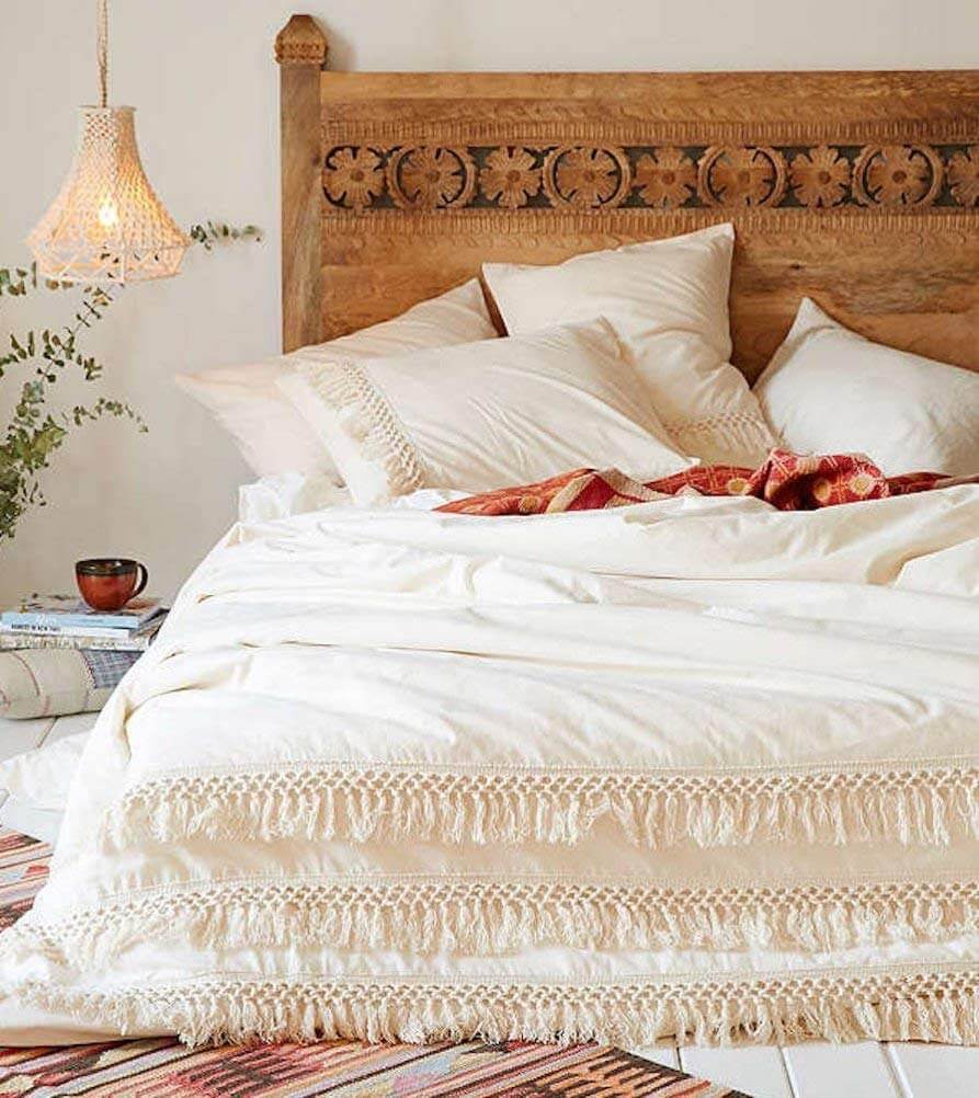 Messy white bed with Urban Outfitters headboard and fringed comforter