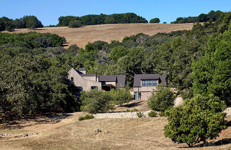 Modern farmhouse seen on the side of a hill with trees