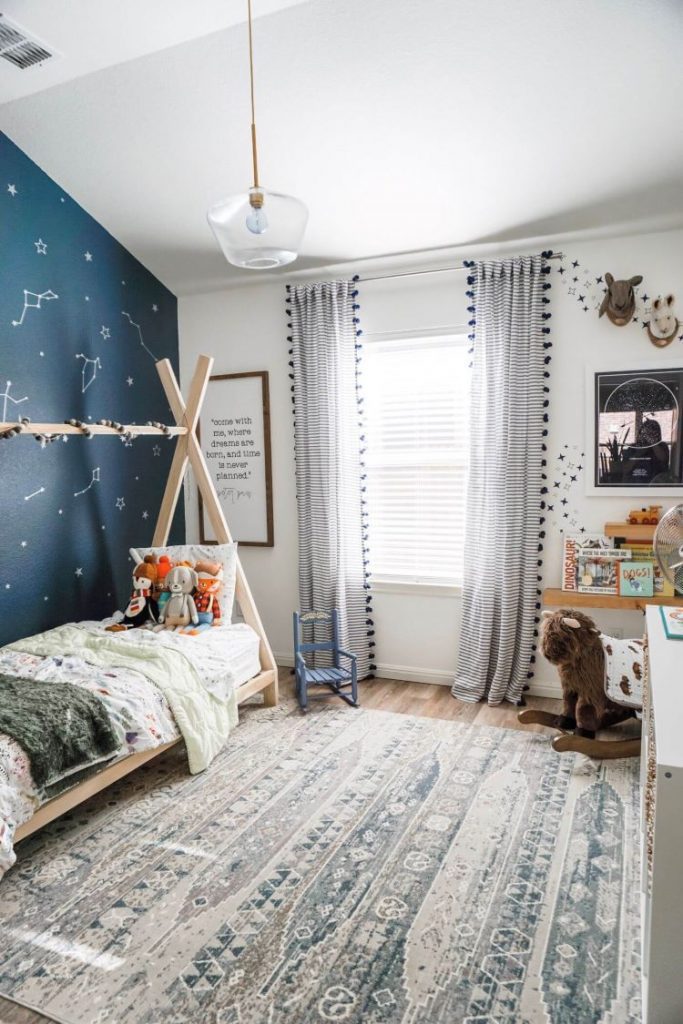 A boy'd bedroom with a blue accent wall covered in vinyl star stickers. There is also a tepee bed and a child's rocking chair