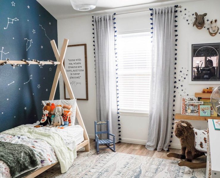 A boy's bedroom with a blue accent wall covered in vinyl star stickers. There is also a tepee bed and a child's rocking chair