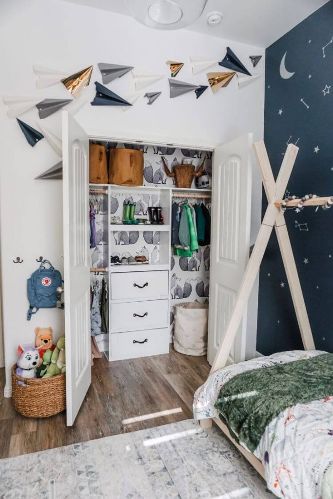 Above the boy's closet are pinned several paper airplanes in gold, grey, blue and white to match the rest of the room's colors