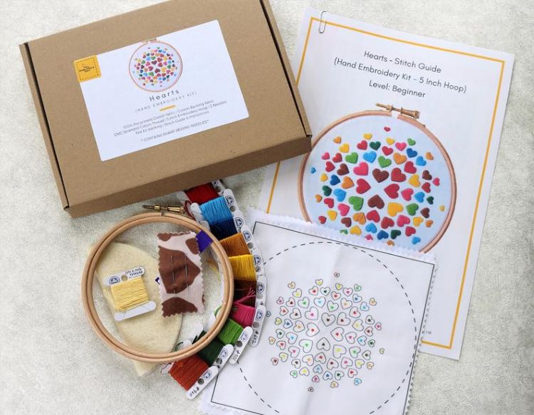 A box and supplies that will make a stitched rainbow heart embroidery