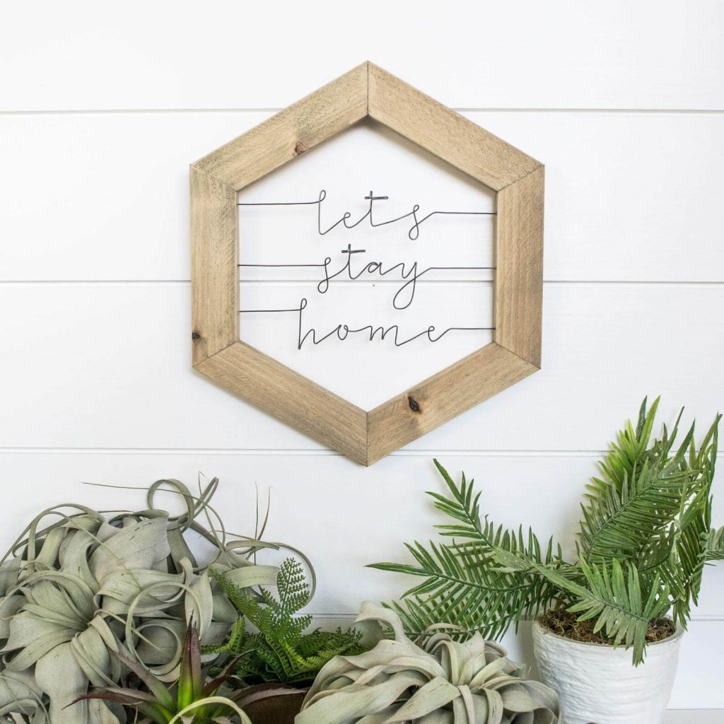 Geometric wood frame with words made from metal wire inside saying "Let's Stay Home"