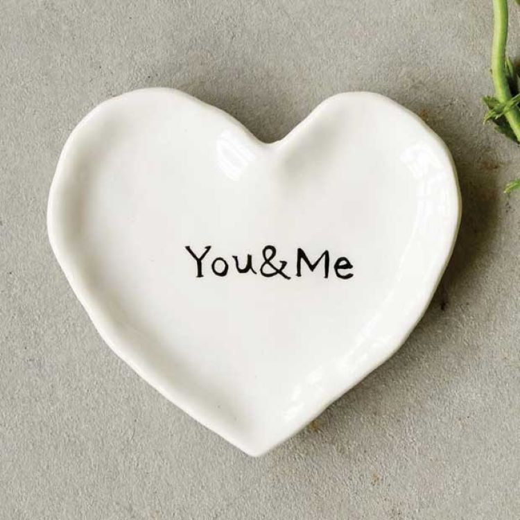 A white ring dish shaped like a heart. Painted inside are the words, "You and Me"