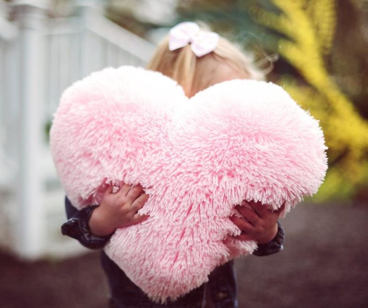 A little girl cuddles a fluffy pink pillow