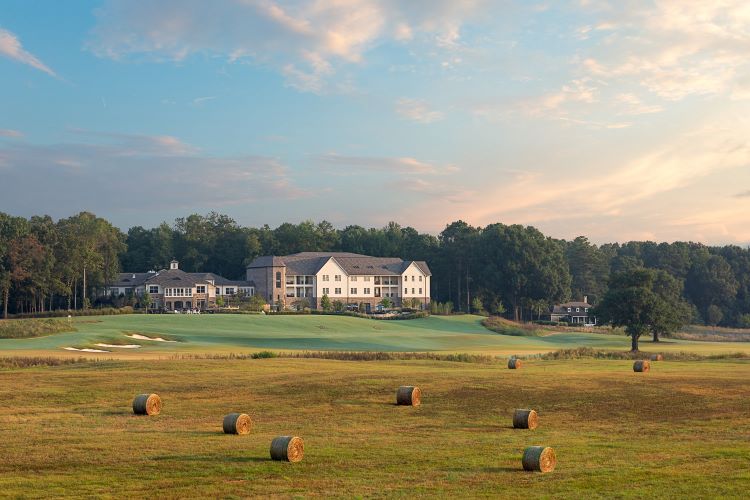 A large field full of hay bales in front of a massive large white building that is the hotel