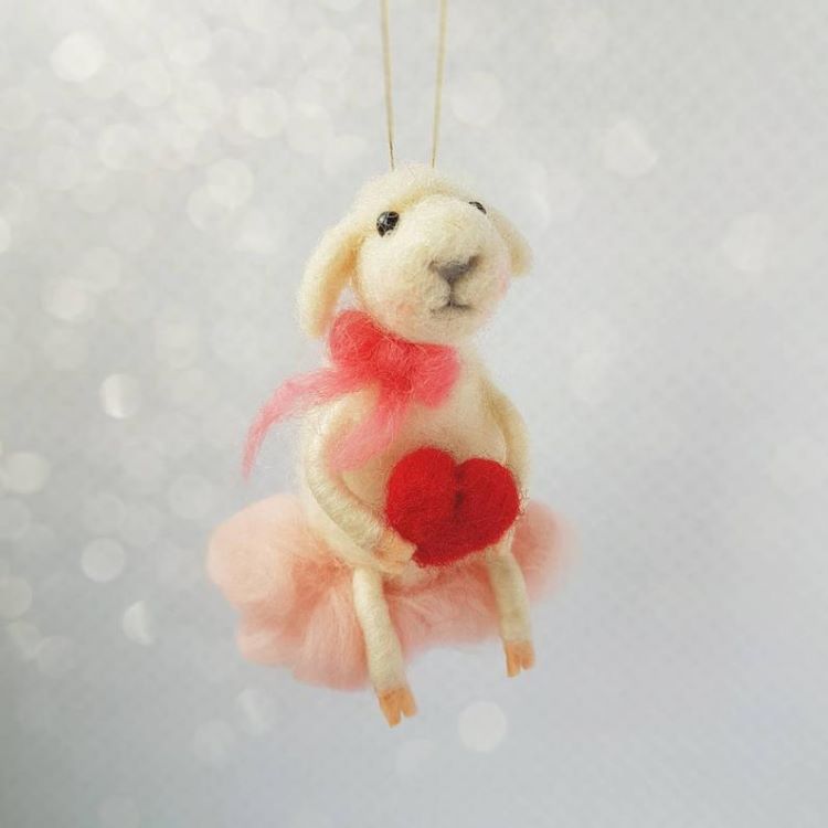 A felted lamb ornament holding a heart and wearing a pink bow
