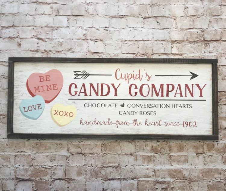 Sign art saying "Cupid's candy company." with images of conversation hearts