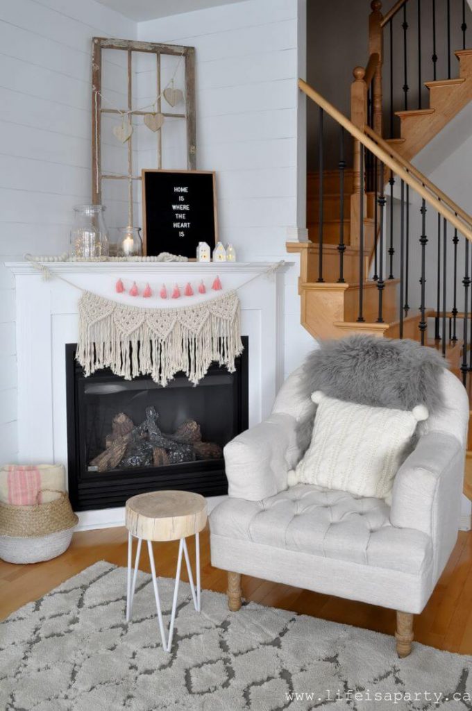 A pink tassel garland adorns a white farmhouse fireplace. On the mantel are tiny light up houses made of porcelain normally used for Christmas decorations