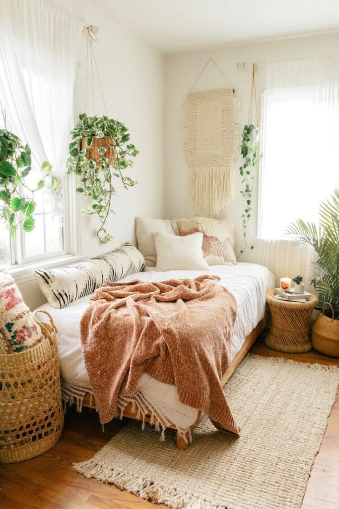 Boho farmhouse style bedroom with hanging plants and rust colored blanket