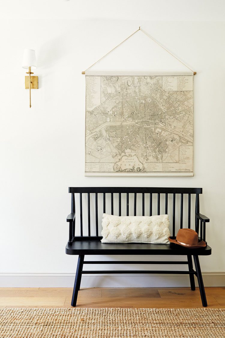 A black bench rests under an antique map on the wall