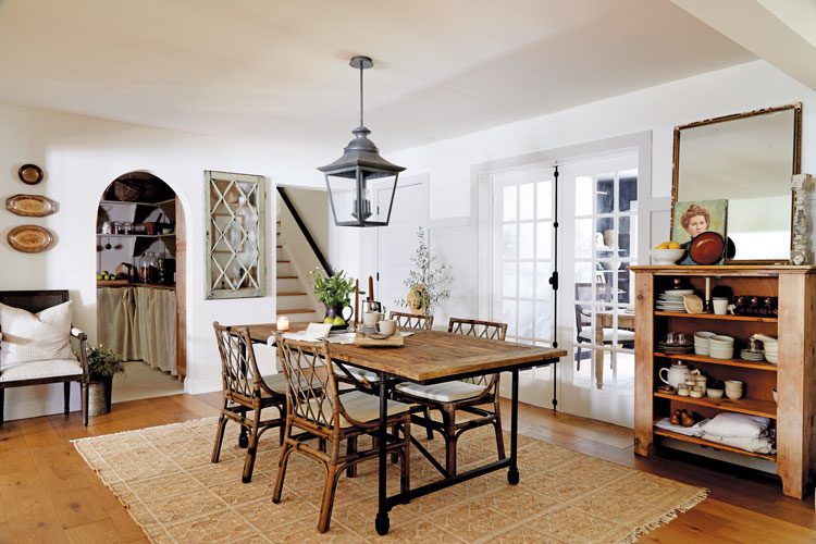 The dining room has a yellow and white rug in intricate small details and patterns, adding a neutral motif to the bookshelf full of cups, teapots and plates.