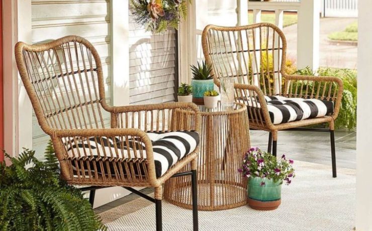 A pair of sand-colored rattan chairs have blacka nd white stripe throw pillows in them on a farmhouse style porch