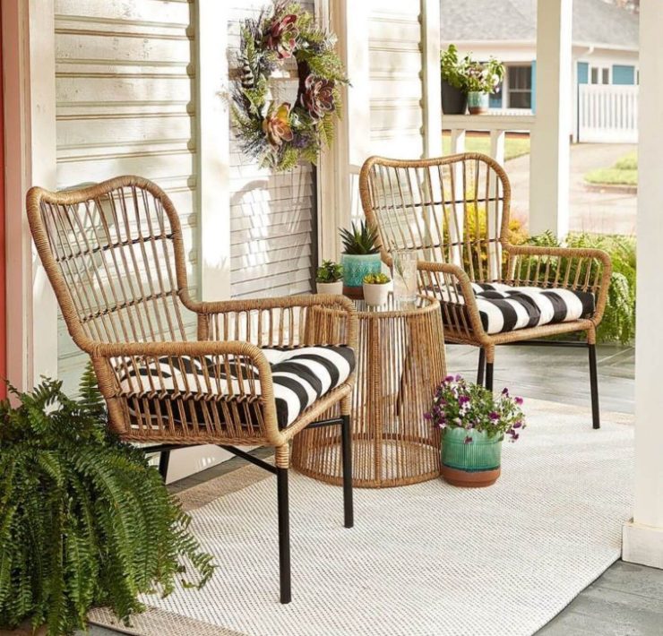A pair of sand-colored rattan chairs have blacka nd white stripe throw pillows in them on a farmhouse style porch