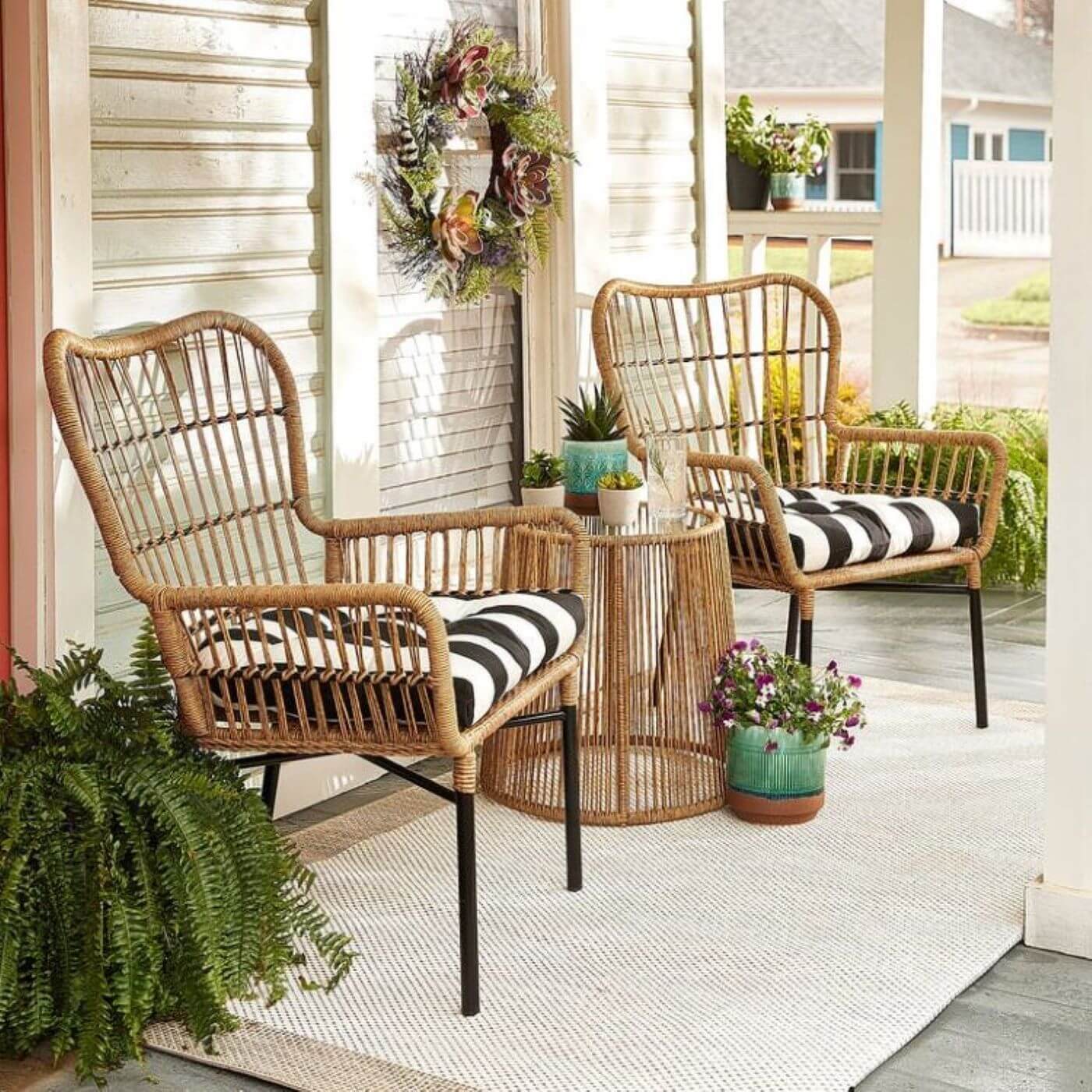 A pair of sand-colored rattan chairs have blacka nd white stripe throw pillows in them on a farmhouse style porch