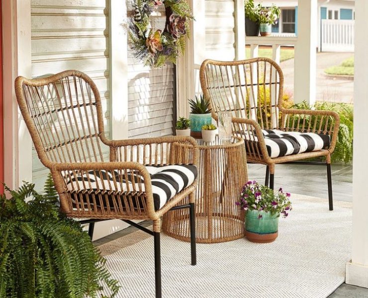 A pair of sand-colored rattan chairs have blacka nd white stripe throw pillows in them on a farmhouse style porch