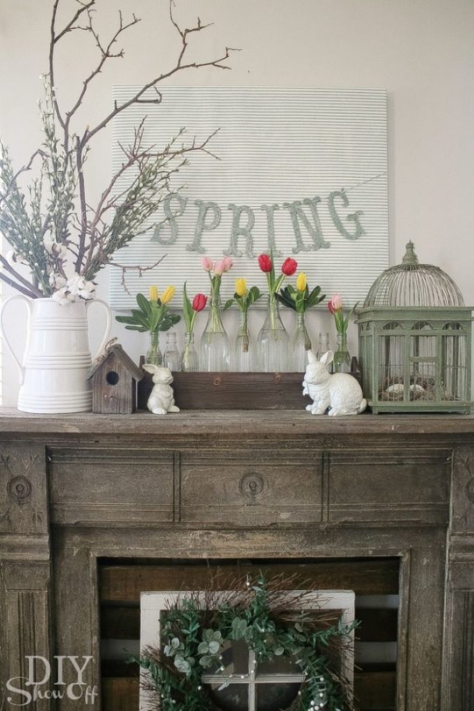 A faux fireplace is adorned with ceramin white bunnies and a vintage bird cage with a row of clear glass bottles full of tulips