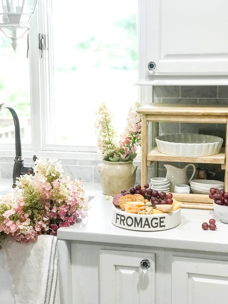 A bright white farmhouse style kitchen countertop with a bouquet of summer decor flowers. The flowers are white, pink and purple snap dragons