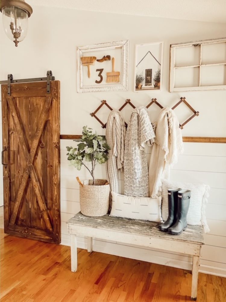 An entryway with a wall coat hanger which has several white and off-white throws above a mini bench in white chippy paint.