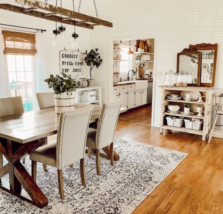 A dining room with a wood floor and a vintage style rug under a table and set of chairs. Above the table is a chandelier made with lights strung through a flea market painter’s ladder.