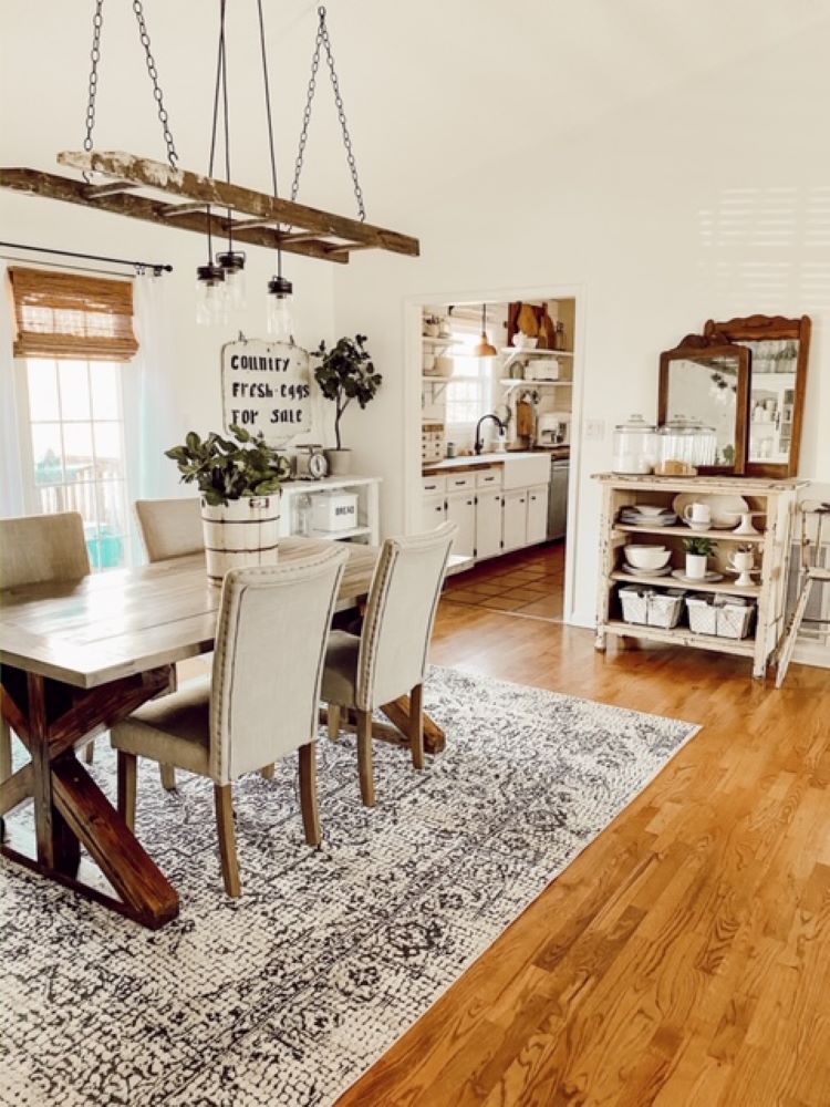 A dining room with a wood floor and a vintage style rug under a table and set of chairs. Above the table is a chandelier made with lights strung through a flea market painter’s ladder.