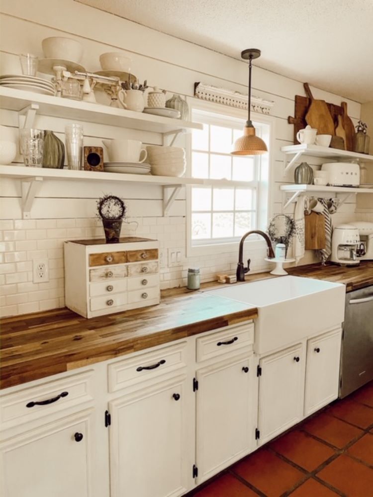 The kitchen has countertops made from butcher block in a rich warm wood tone. The backsplash is white tile and the lower cabinets are painted white as well.