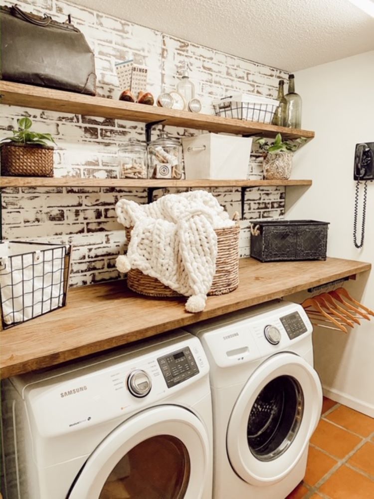 The laundry room has a brick wall behind the laundry machines. The brick is made from brick paneling. Open shelves hold laundry and accessories for doing the chore.