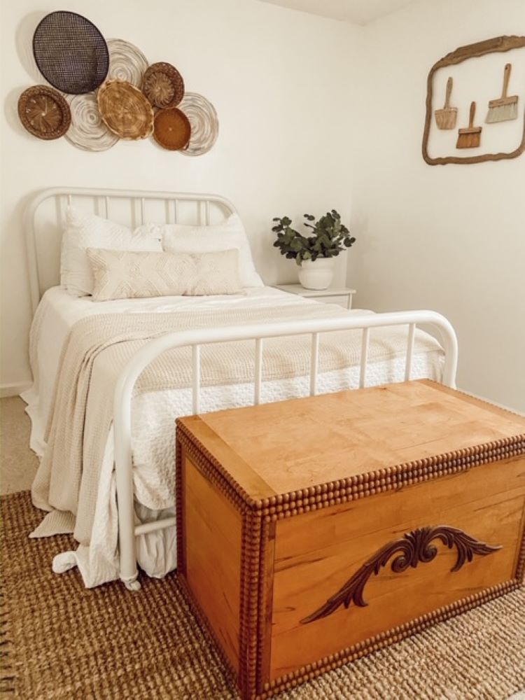 A white bedroom with framed paintbrushes on the wall next to a bed in a wire frame.