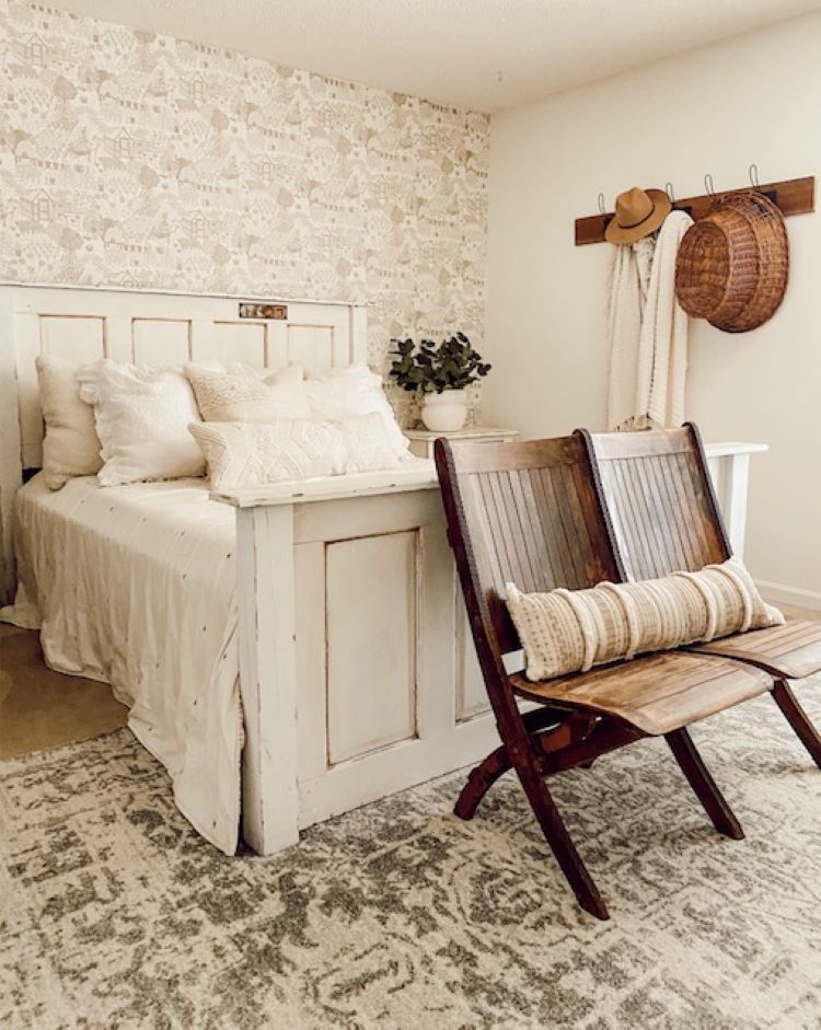 A white room with an accent wall behind the bed made from eighteenth-century doors from the Facebook marketplace. The accent wall is layered in wallpaper with a pattern of farmhouses and other pastoral features.