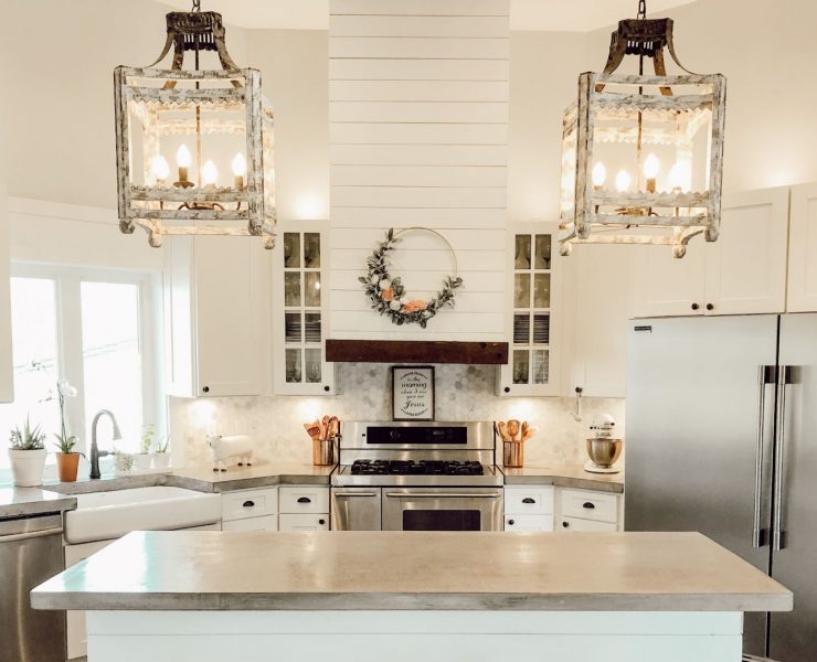 A white farmhouse kitchen with poured concrete countertops and white shiplap beside two large pendant lights