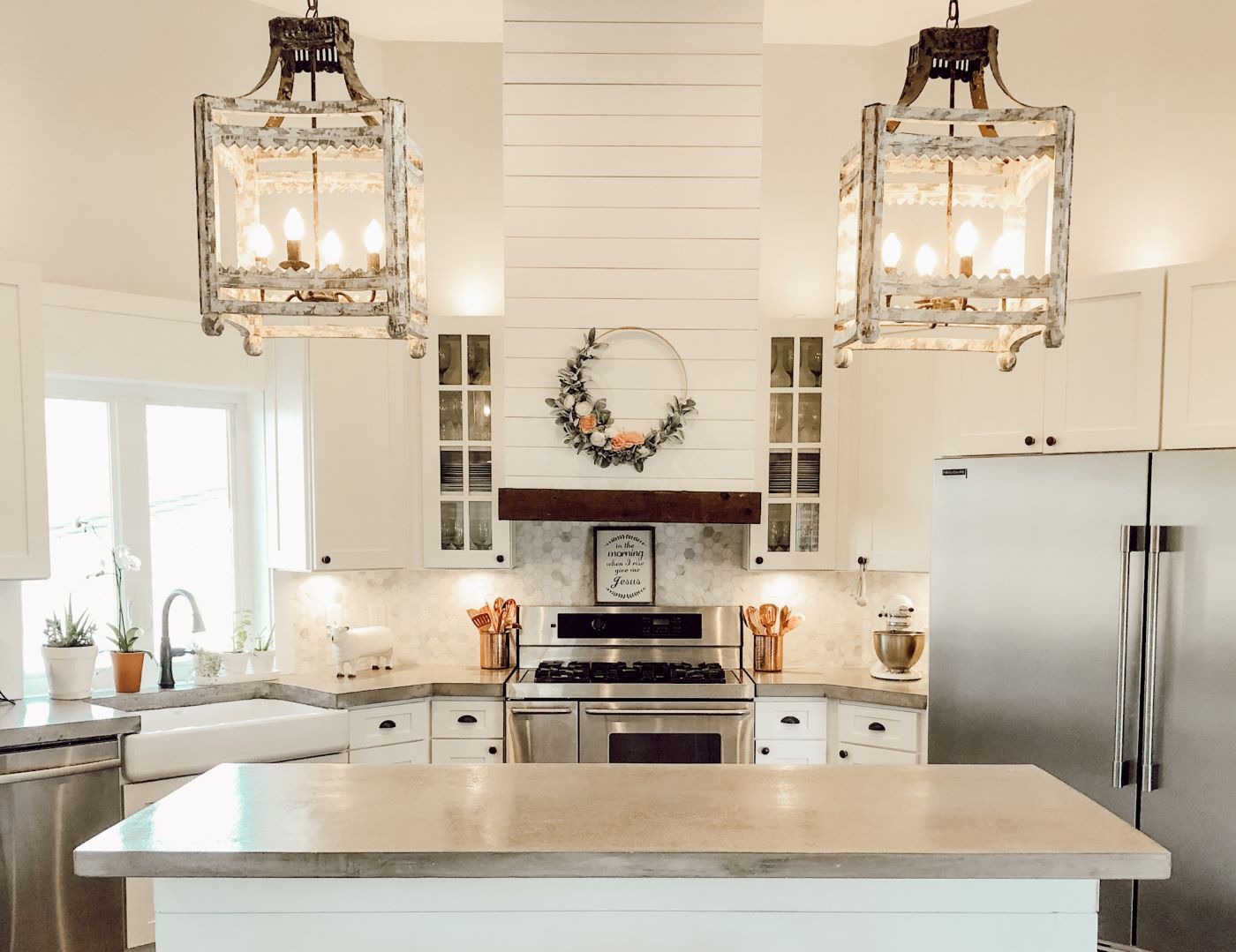 A white farmhouse kitchen with poured concrete countertops and white shiplap beside two large pendant lights