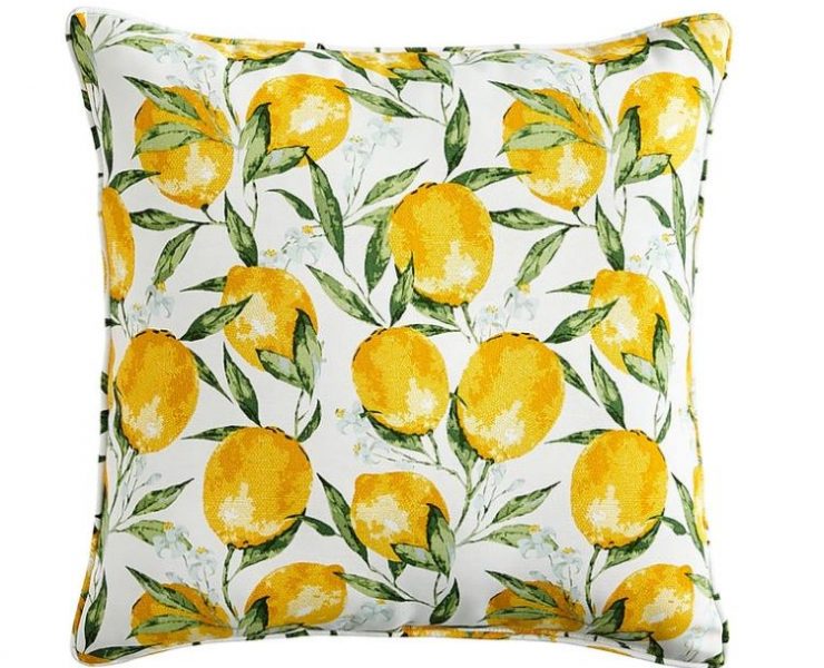 A throw pillow with a white background covered in bright yellow lemons and green leaves