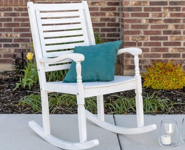 A white rocking chair in a classic farmhouse style has a teal throw pillow in its seat