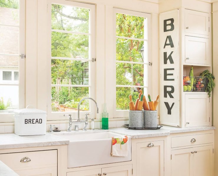A kitchen painted in sage green on the walls and white cabinets and clean countertops. a large sign says Bakery near the clear windows.